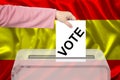 Female voter drops a ballot in a transparent ballot box against the background of the national flag of Spain, concept of state Royalty Free Stock Photo