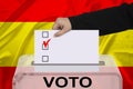 Female voter drops a ballot in a transparent ballot box against the background of the national flag of Spain, concept of state Royalty Free Stock Photo