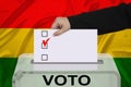 Female voter lowers the ballot in a transparent ballot box against the background of the national flag of bolivia, concept of