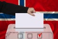 Female voter lowers the ballot in a transparent ballot box against the background of the national flag of Norway, concept of state