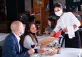 Female waitress in mask taking order from female and male customers in cafe Royalty Free Stock Photo