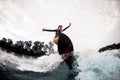 Female wake surfer in black wetsuit rides up on surf board on wave Royalty Free Stock Photo