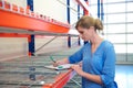 Female warehouse employee standing next to shelves and writing on clipboard