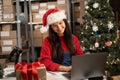 Female warehouse inventory manager using laptop computer and checking retail stock. Happy woman wear Santa hat working Royalty Free Stock Photo