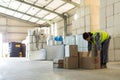 Female warehouse worker stacking boxes on warehouse floor with barrels and crates, copy space Royalty Free Stock Photo