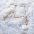 Female white heart shaped agate pendant with golden chain on white snow background