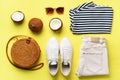 Female white sneakers, jeans, striped t-shirt, rattan bag, coconut and sunglasses on yellow background with copy space