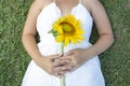 Female in a white summer dress lying on the grass with a sunflower in her hands