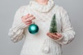 Female in a white sweater holding a turquoise Christmas ball and miniature pine tree