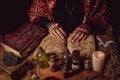 Female witch making potion on dark background, magic bottles with potions and candles on table of alchemist, Halloween theme