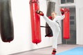 Female woking out karate raising leg and boxing heavy bag in gym.