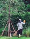 Female worker cleaning up leaves with traditional broom tool in ornamental garden. Woman wear rubber gloves with hat and boots