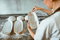 Worker pours flour inside dish to bake bread at table in light workshop