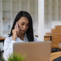 Female worker talking on the phone while woking with laptop in office room Royalty Free Stock Photo