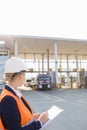 Female worker writing on clipboard while looking at trucks entering in shipping yard