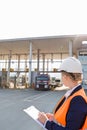 Female worker writing on clipboard while looking at trucks entering in shipping yard