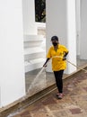 A female worker with yellow shirt and face mask is cleaning the grounds with a water hose at the Wat Pho temple in Bangkok, Royalty Free Stock Photo