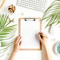 Female workspace with female hands, clipboard, tropical palm leaves, computer, accessories on white background. Stylized