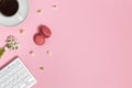 Female workspace with keyboard, cup of black coffee, macarons and daisy flowers on pink background, top view