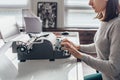 Female writer typing on a typewriter sitting in her workroom.