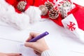 Female writing wish list in notebook near christmas gifts Royalty Free Stock Photo