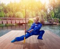 Female wushu fighter with blade against lake