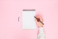 Female hand writing in white blank open spiral notebook with pen isolated on pastel pink background. Flat lay, copy space Royalty Free Stock Photo