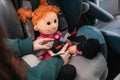 Female& x27;s hands fasten the seat belts on a plush doll sitting in a child& x27;s seat