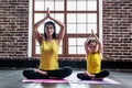 Female yoga instructor training little girl doing stretching exercise sitting in lotus position indoors