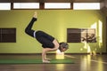 A female yoga practitioner doing a variation of the Eka Pada Bakasana exercise, handstand with leg extended, exercising on a mat