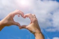 Female young hands in heart shaped gesture on blue cloudy sky background and bright sunlight. Concept of love sicking, relationshi Royalty Free Stock Photo