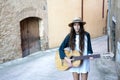 Young girl musician in summer clothes on walking on antique street while playing acoustic guitar Royalty Free Stock Photo