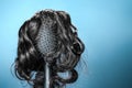 Females hair. Black hairbrush with a black wig, looks like a woman's head with a hairstyle. Blue background. Copy space. Royalty Free Stock Photo