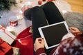 Females legs with tablet next to Christmas tree