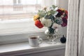 Feminine autumn still life. Cup of coffee, bouquet of colorful dahlia flowers in glass vase on windowsill. Styled moody