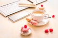 Feminine business workplace with keyboard, writing supplies, cup of coffee and small macarons
