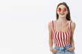 Feminine and confident female internet blogger in trendy sunglasses and pin-up striped top holding hand in pockets of