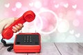 A feminine elegant beautifully manicured woman`s hand holding an old red telephone handset over an abstract blurry light pink Royalty Free Stock Photo