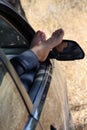 Feminine feet outside car window, enjoying shade in the countryside.