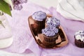 Feminine floral background. Purple cupcakes on the golden tray and bouquet of lilac flowers