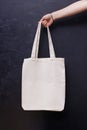 Feminine hand holding canvas tote bag over the black wall