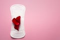 Feminine hygiene pad with red glitter and rose flower. First menstrual period concept on pink background