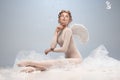 Portrait of pretty, slim beautiful young girl, graceful ballerina in image of angel with wings sitting on cloud 