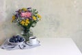 Feminine wedding, birthday scene with cup of coffee and plum fruit bowl. Glass vase with beautiful colorful bouquet of