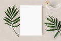 Feminine wedding stationery mock-up scene. Blank greeting card, green palm leaves and silk ribbon on beige textured