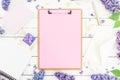 Feminine work place composition with clipboard, notebook, lilac flowers, gift box and accessories on rustic background. Flat lay,