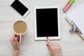 Feminine work space with tablet, noticepad, sheet, latte ice, smartphone and female hands over white wooden background, top view.