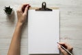 Feminine workspace with female hands, clipboard and sheet of paper, overhead. Top view