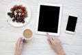 Feminine workspace with female hands, smartphone, tablet, berries and latte on white wooden background, top view. Flat lay. Royalty Free Stock Photo