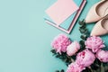 Feminine workspace with notebook, shoes, pink peony, eucalyptus flower on blue background. Top view, copy space. Blogger, feminine